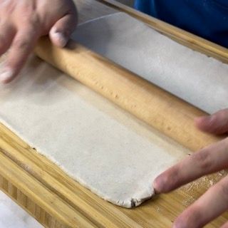 Una persona sta stendendo la pasta con un mattarello di legno