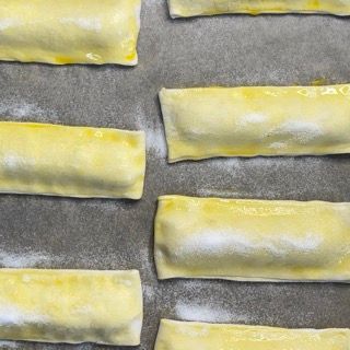 Un mucchio di rotoli di pasta sfoglia sono allineati su una teglia da forno.