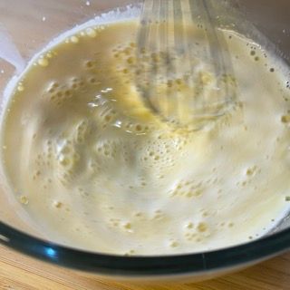 Primo piano di una ciotola piena di liquido con una frusta dentro.