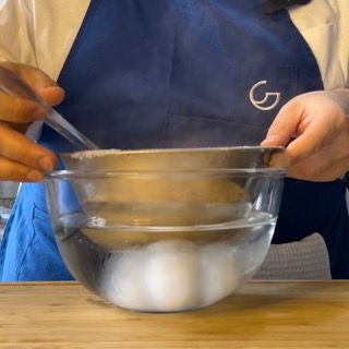 Una persona con un grembiule blu sta mescolando le uova in una ciotola d'acqua