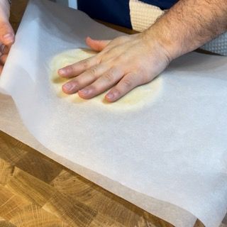 Pasta frolla stesa tra due fogli di carta da forno.
