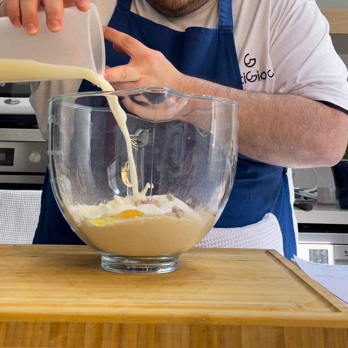 Un uomo con un grembiule che versa del liquido in una ciotola di vetro