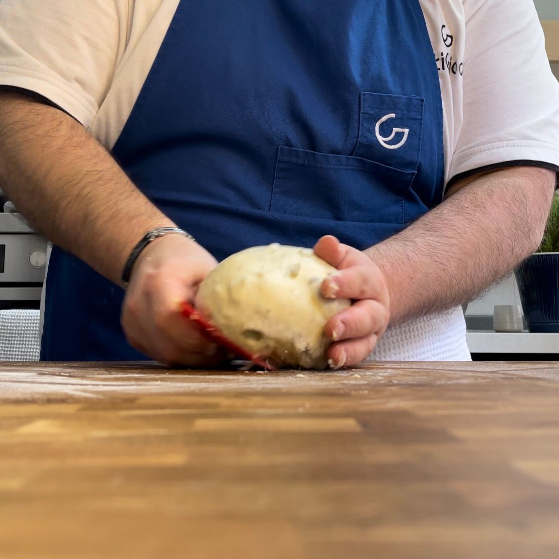 Un uomo con un grembiule blu tiene in mano una palla di pasta