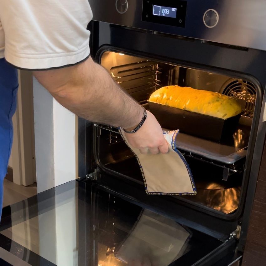 Un uomo sta tirando fuori un pezzo di pane da un forno che ha un orologio sopra