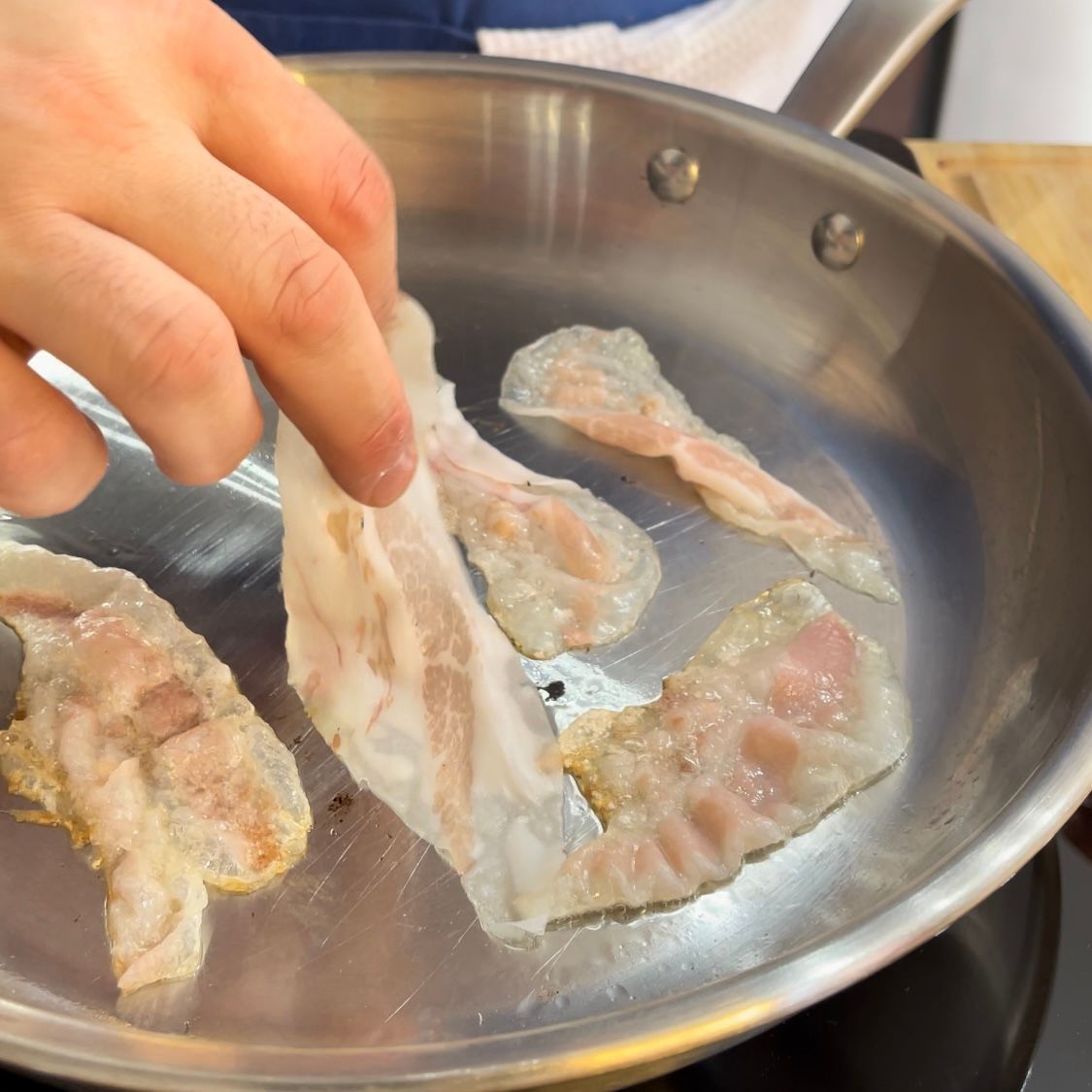 Una persona sta cucinando la pancetta in una padella