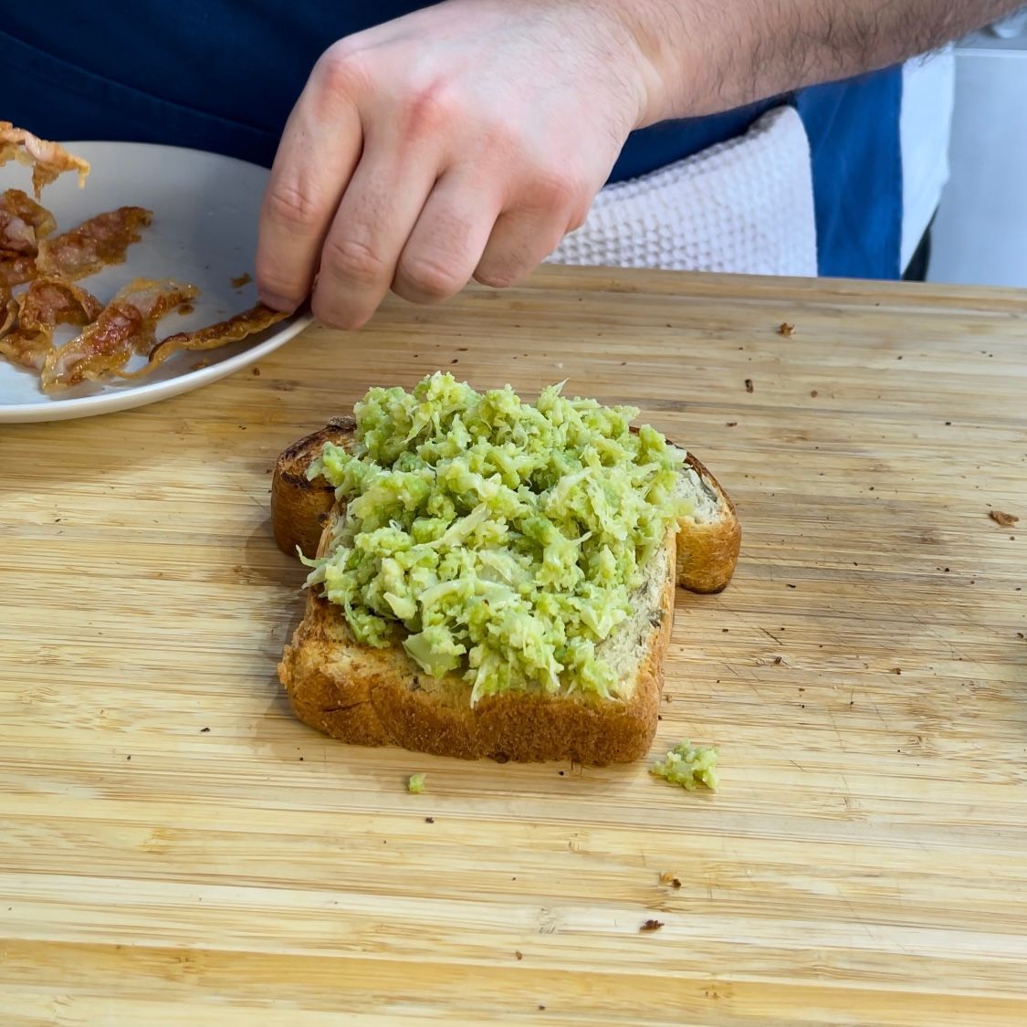 Una persona sta spalmando il guacamole su una fetta di pane su un tagliere.
