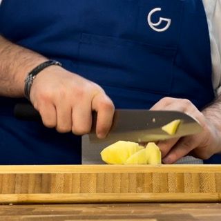 Un uomo con un grembiule blu sta tagliando un ananas su un tagliere