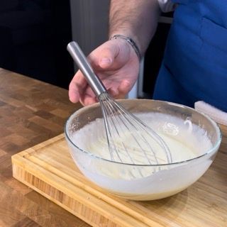 Una persona tiene una frusta sopra una ciotola di panna montata