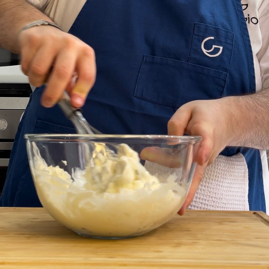 Un uomo con un grembiule sta mescolando qualcosa in una ciotola di vetro