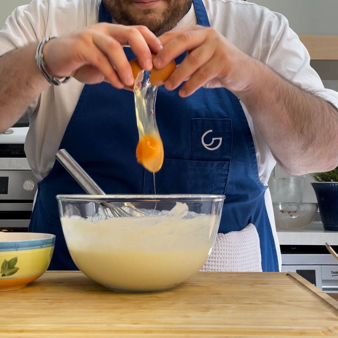 Un uomo con un grembiule rompe un uovo in una ciotola