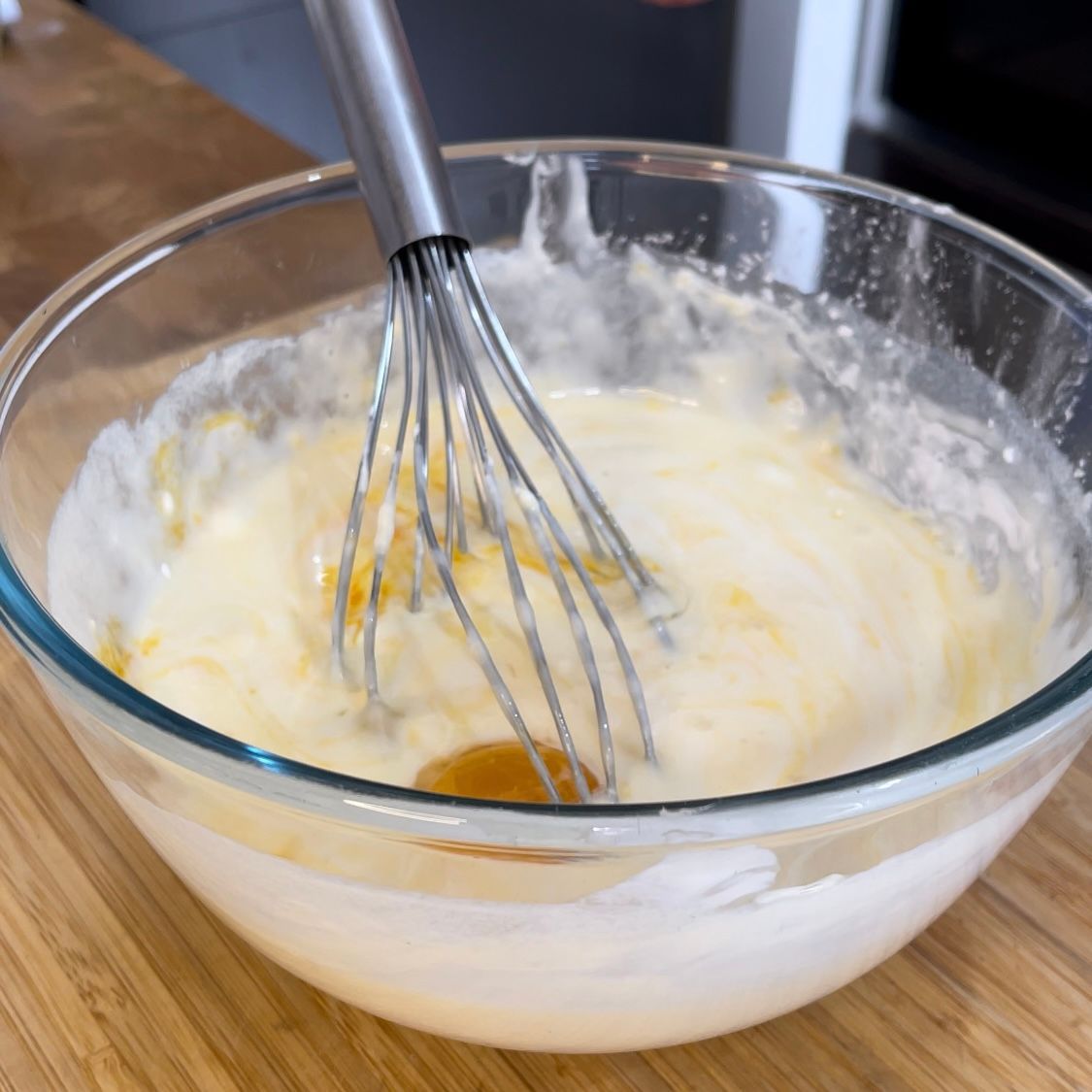Una frusta è in una ciotola di pastella su un tavolo di legno.
