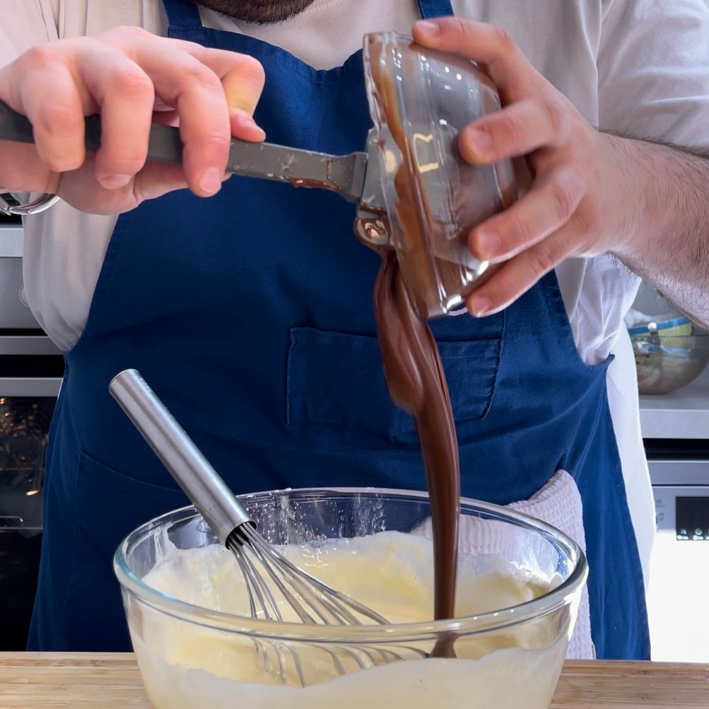 Una persona che versa il cioccolato in una ciotola con una frusta