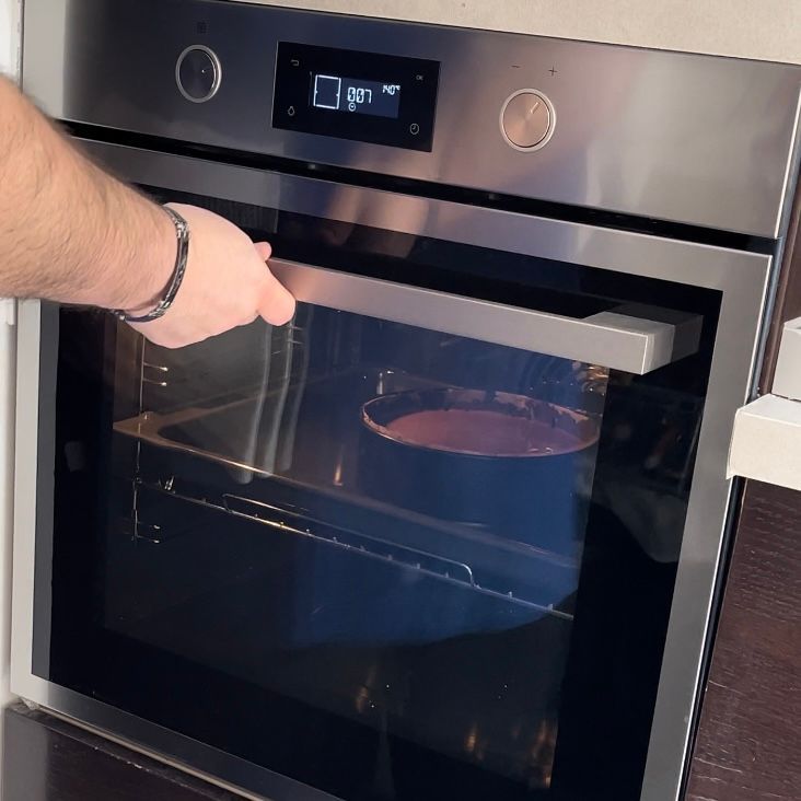 Una persona sta aprendo un forno in acciaio inossidabile con una torta dentro
