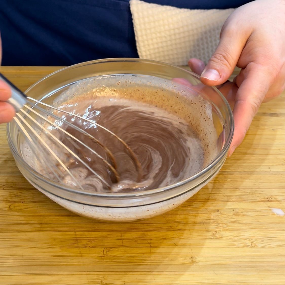Una persona sta mescolando una ciotola di salsa al cioccolato su un tavolo di legno.