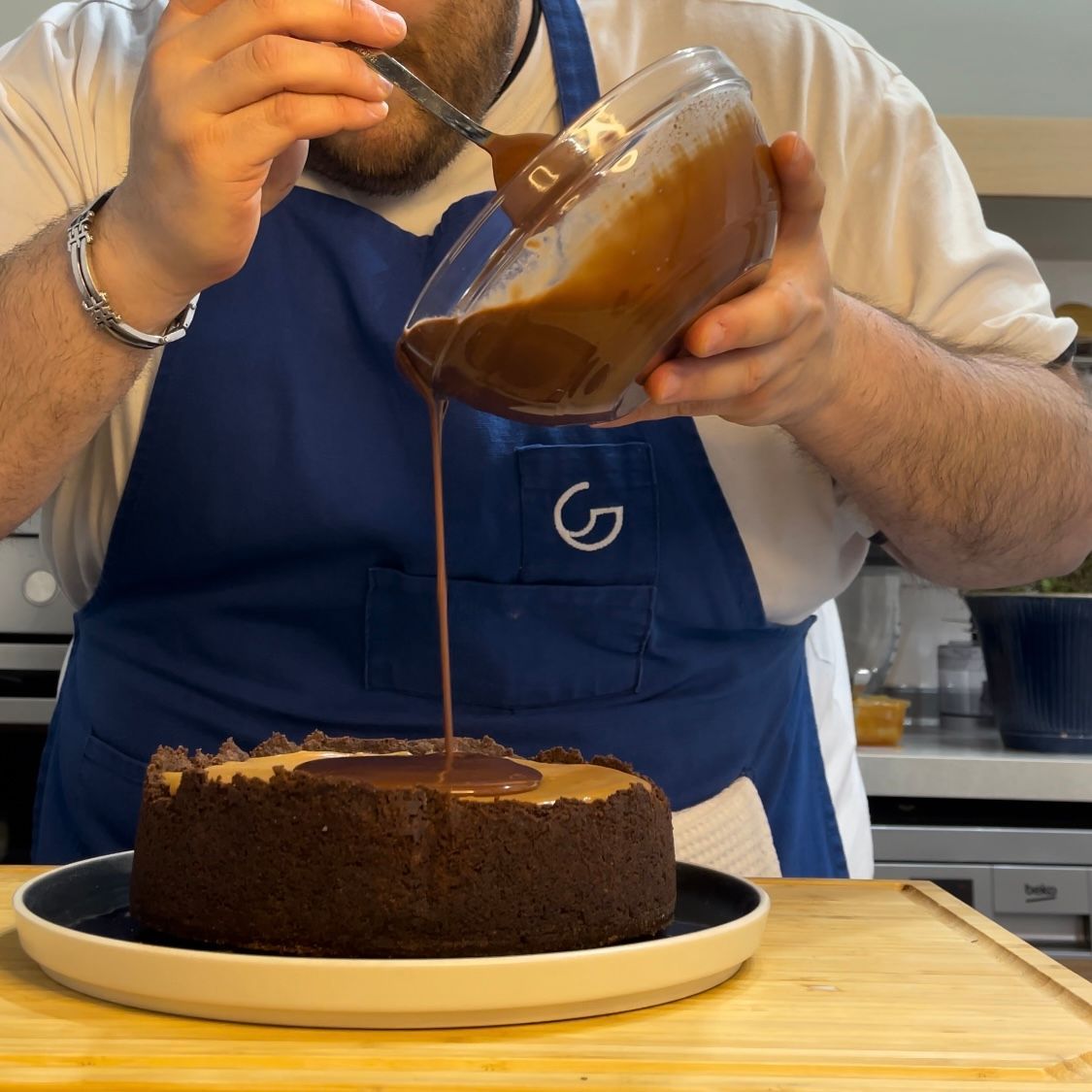Un uomo con un grembiule blu sta versando la salsa al cioccolato su una torta