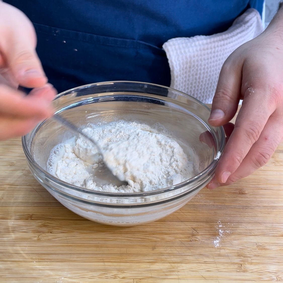 Una persona sta mescolando la farina in una ciotola di vetro con un cucchiaio.