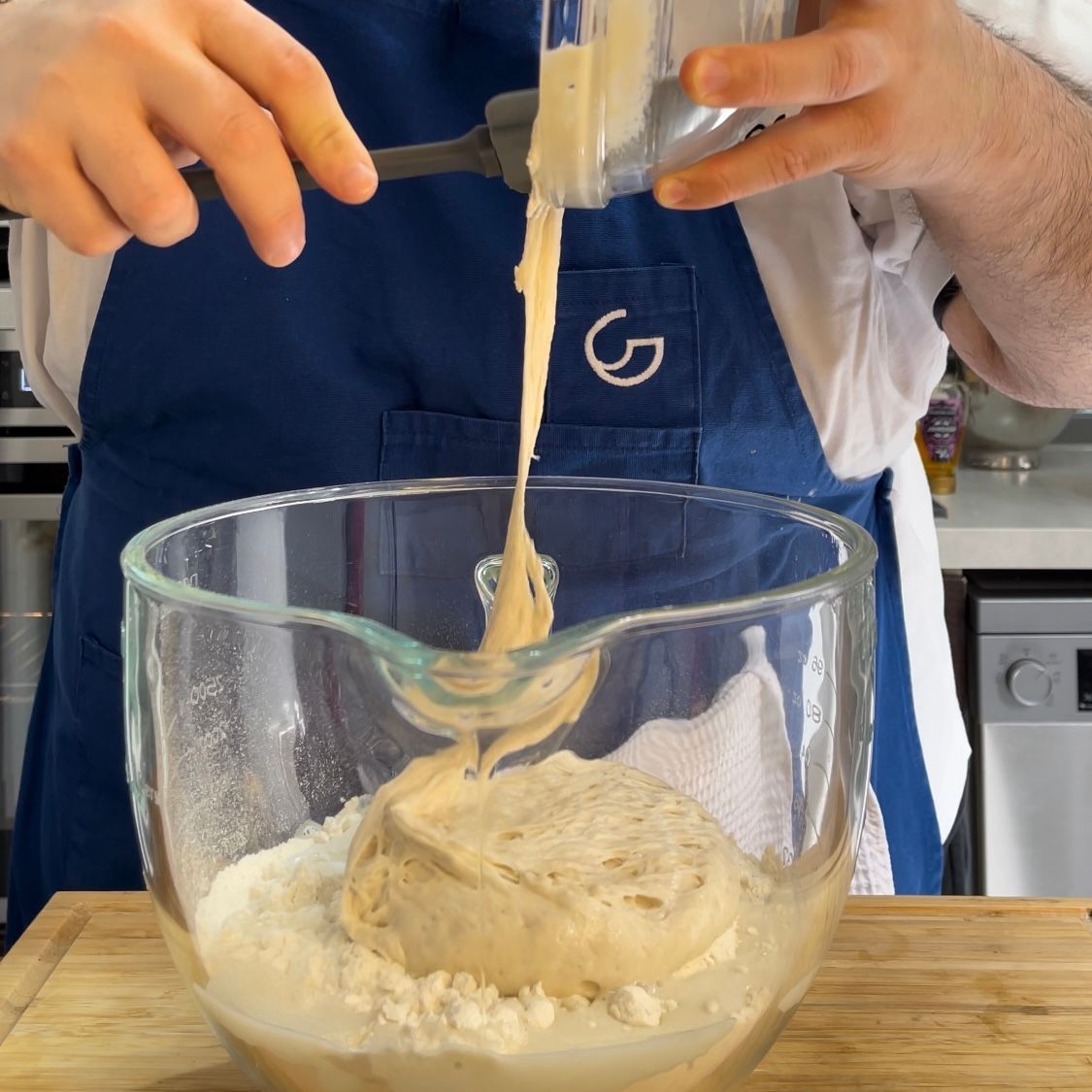 Una persona con un grembiule blu che versa del liquido in una ciotola di vetro