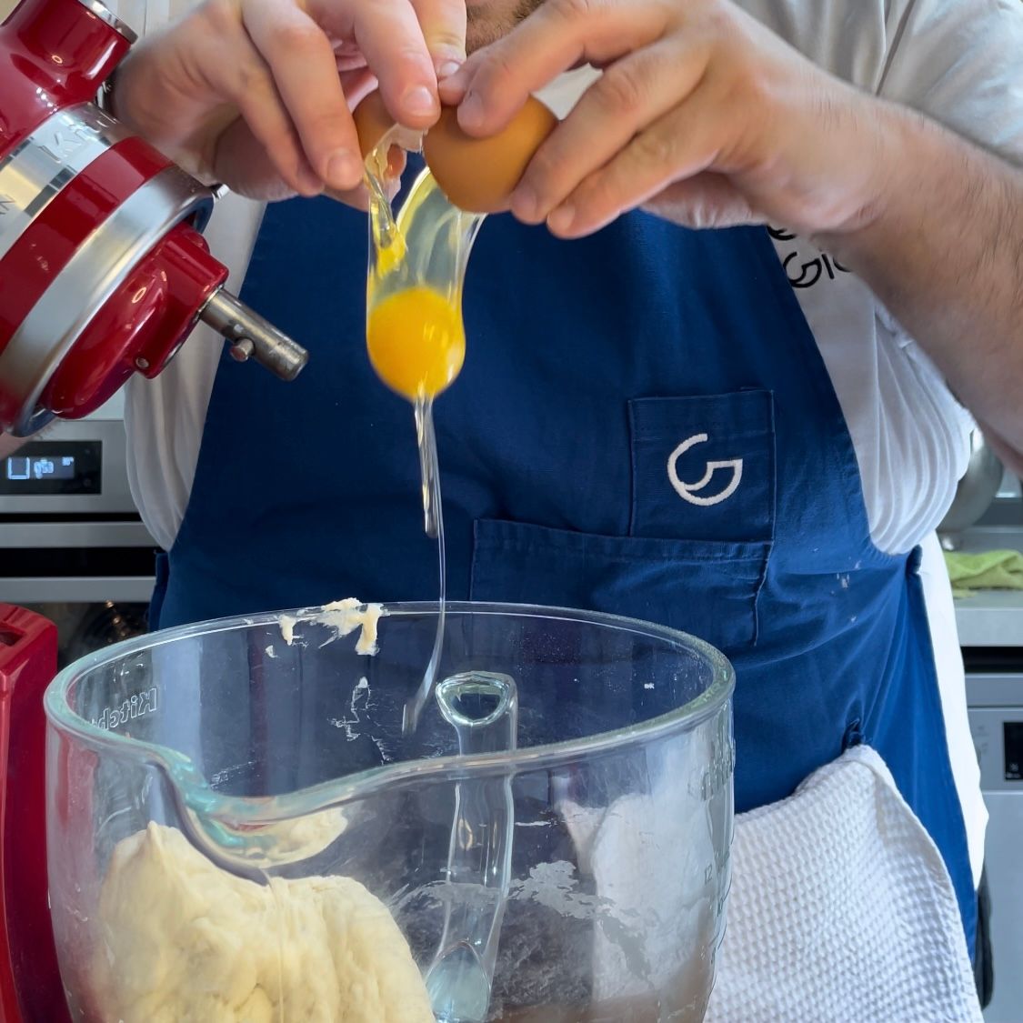 Un uomo con un grembiule rompe un uovo in un bicchiere