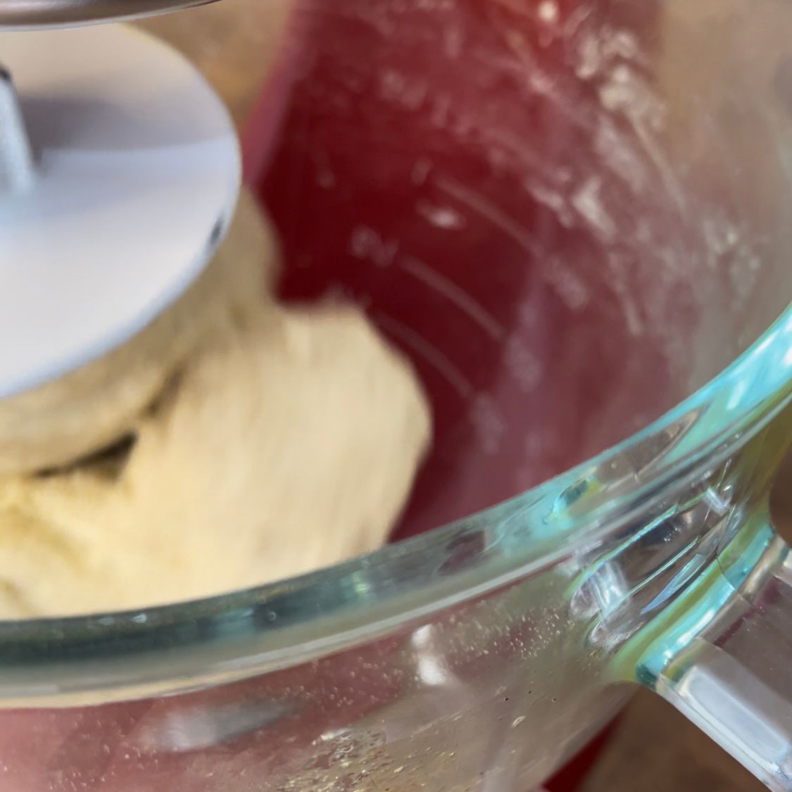 Una ciotola di vetro piena di impasto e un mixer sullo sfondo