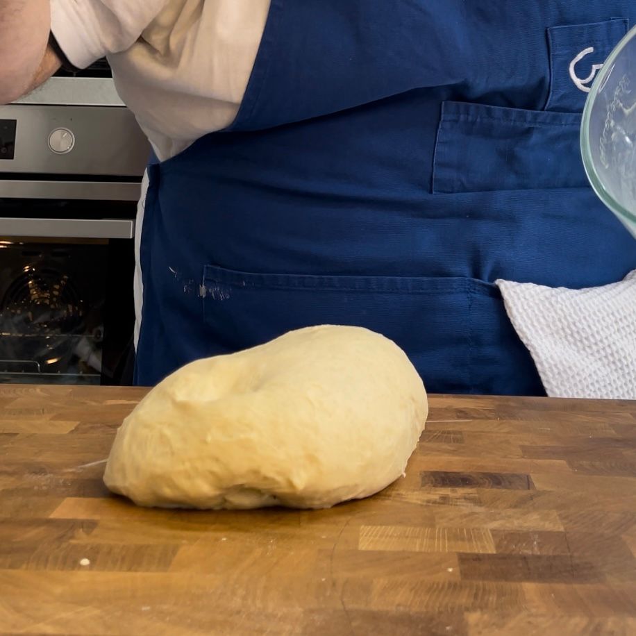 Una persona con un grembiule blu che versa del liquido in una ciotola di vetro