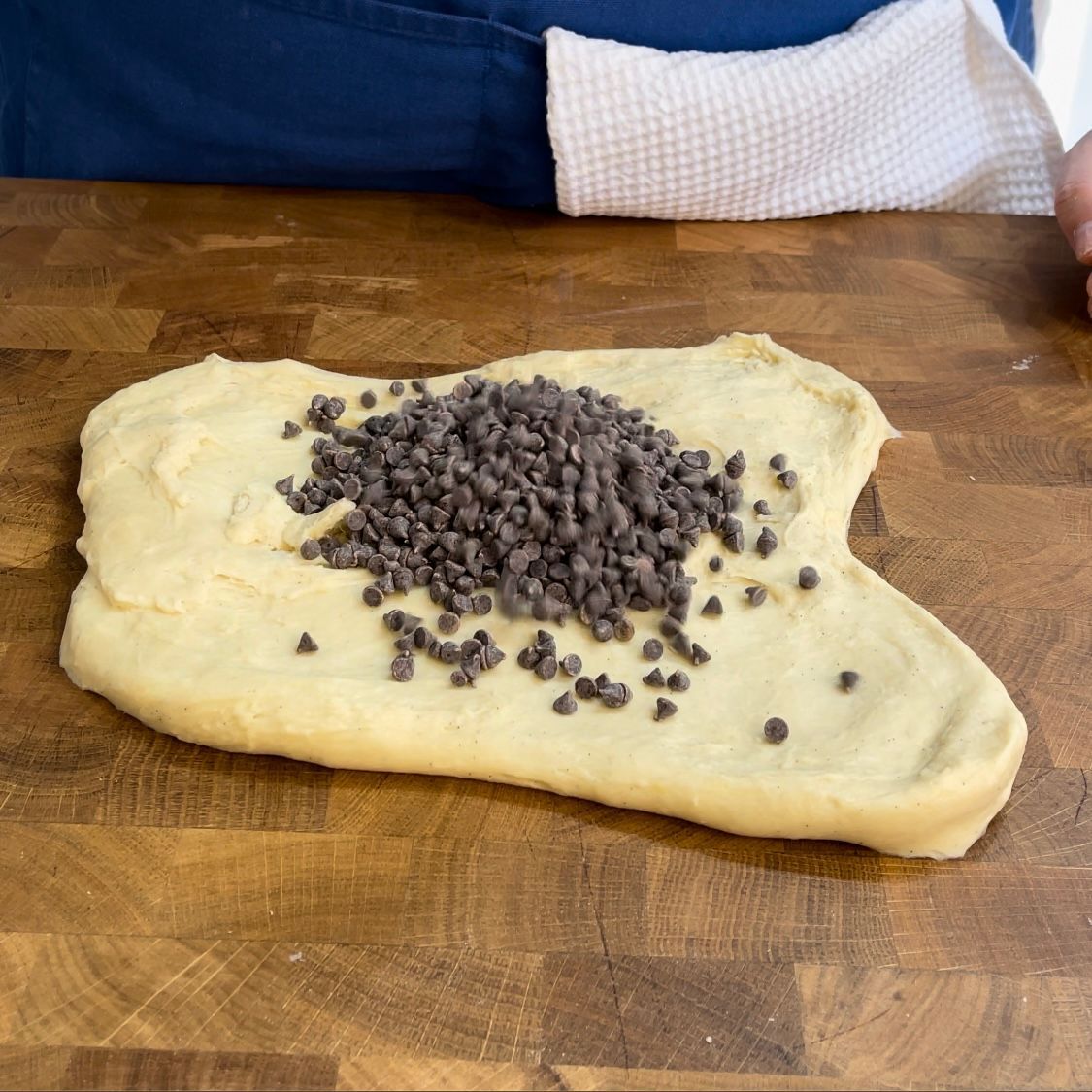 Un pezzo di pasta con gocce di cioccolato sopra su un tagliere di legno.