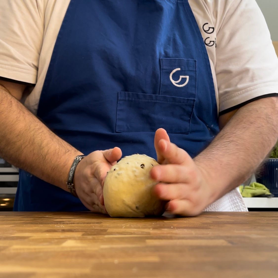 Un uomo con un grembiule blu tiene in mano una palla di pasta