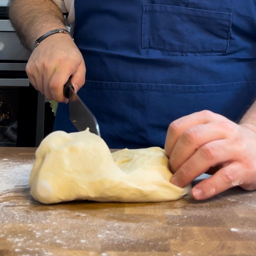 Una persona con un grembiule blu sta tagliando la pasta con una spatola