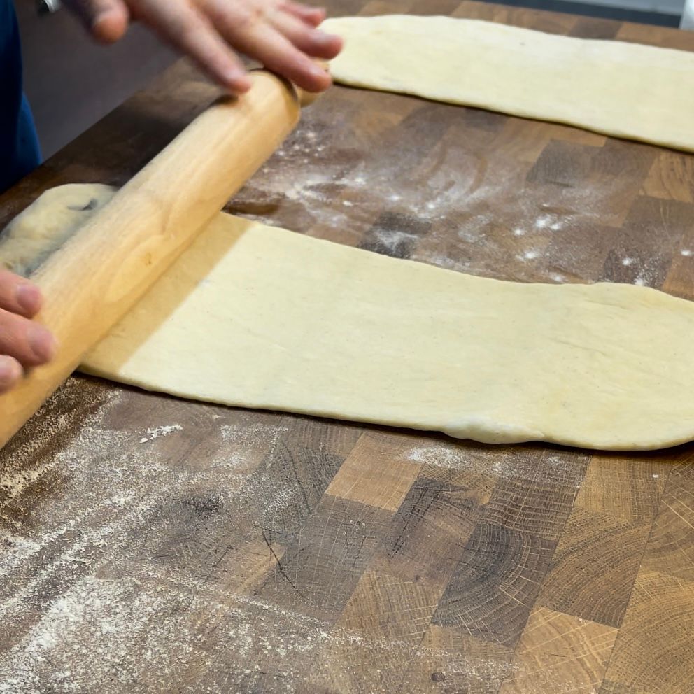 Una persona sta stendendo la pasta con un mattarello di legno