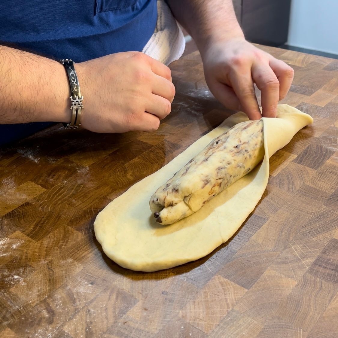 Una persona tiene in mano un pezzo di pasta su un tavolo di legno