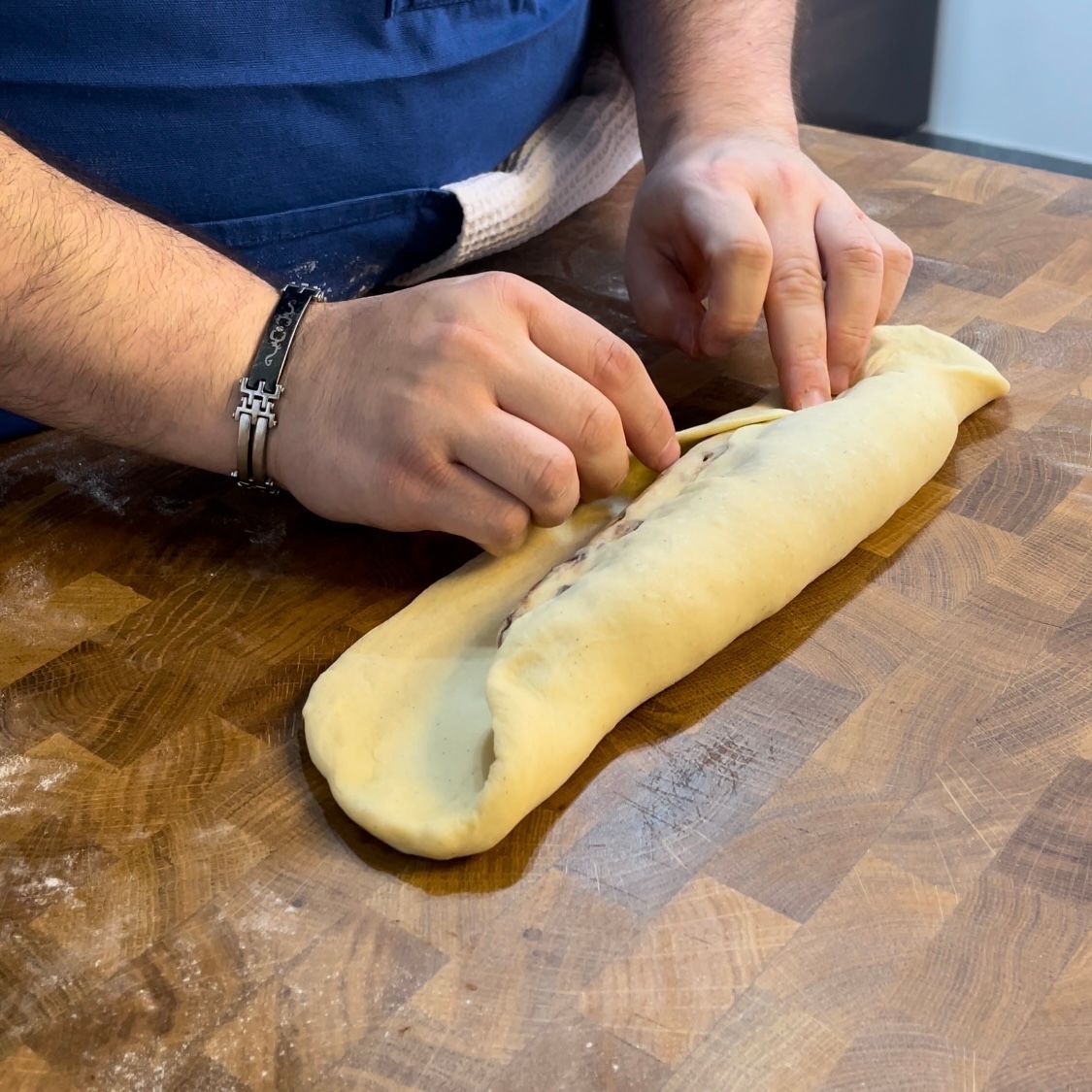 Una persona sta stendendo una pagnotta di pasta su un tavolo di legno.