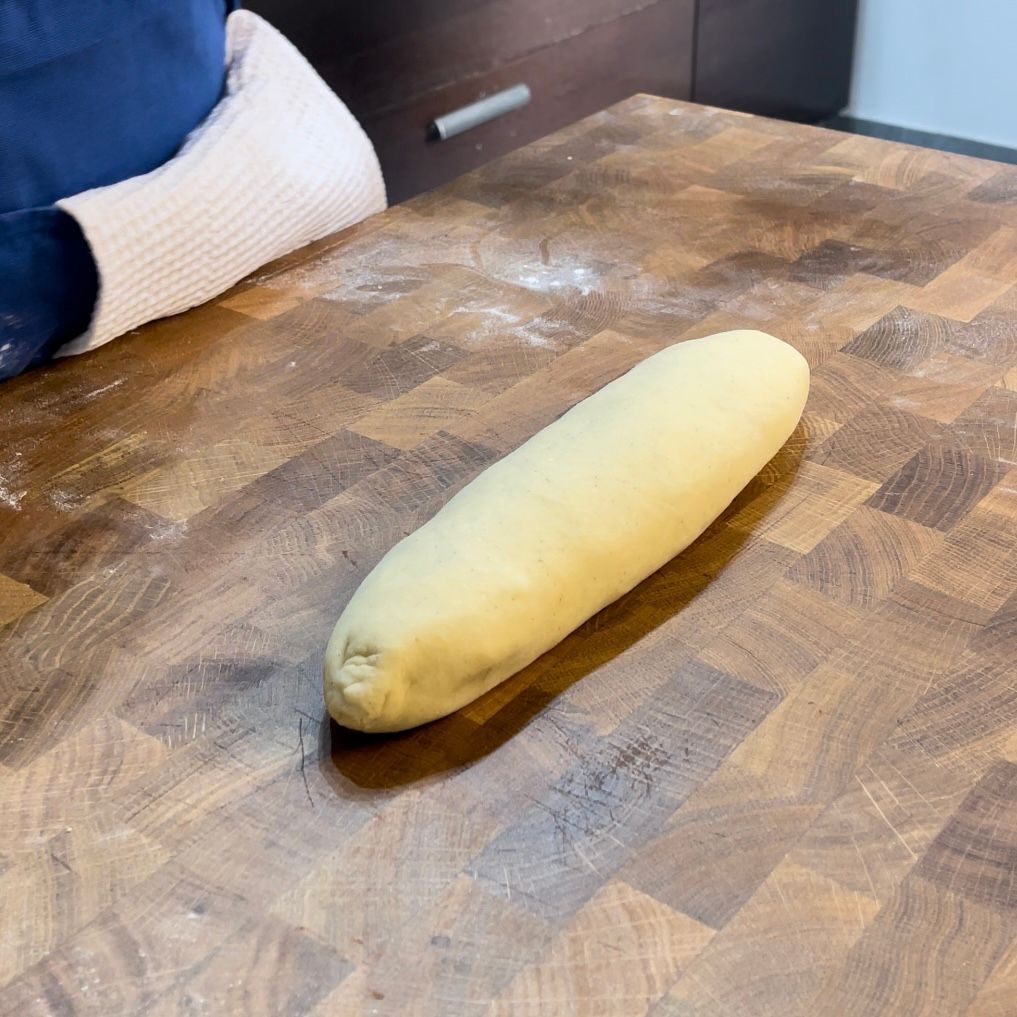 Una pagnotta di pasta è appoggiata su un tagliere di legno.