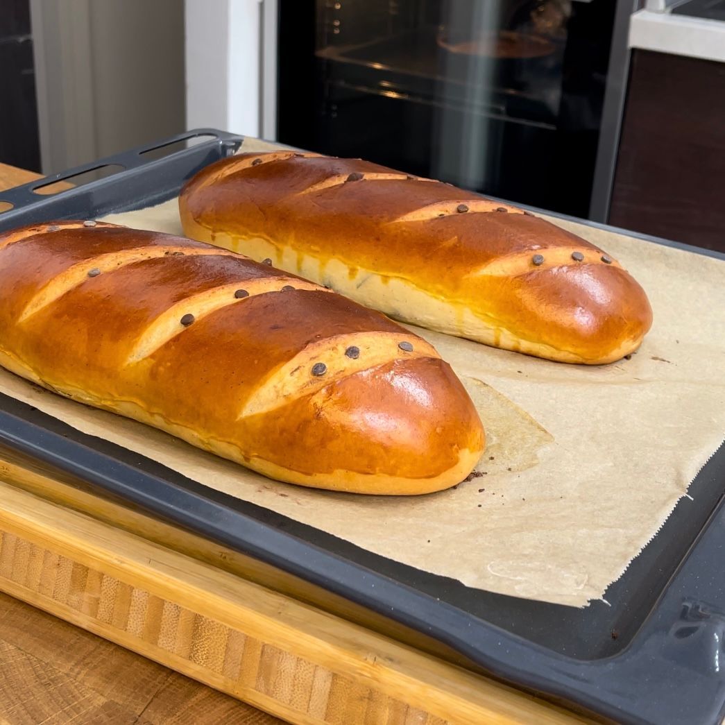 Due pagnotte di pane sono appoggiate su un vassoio sopra un tagliere di legno.