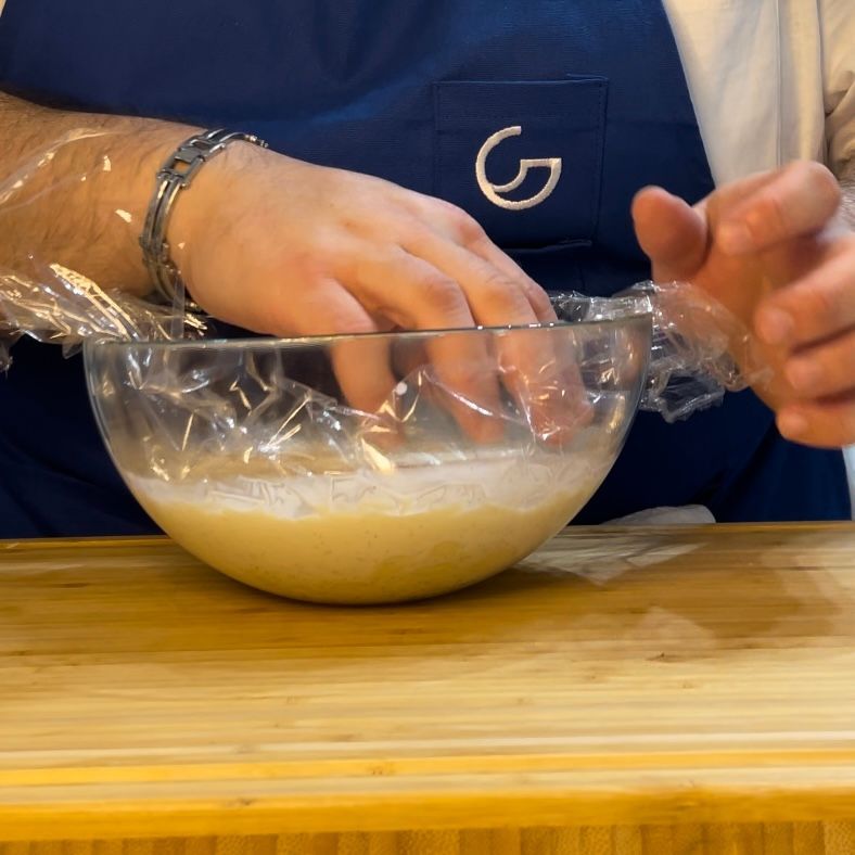Una persona che avvolge una ciotola in pellicola trasparente con ag sul grembiule