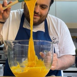 Un uomo con un grembiule sta versando del liquido giallo in una tazza graduata