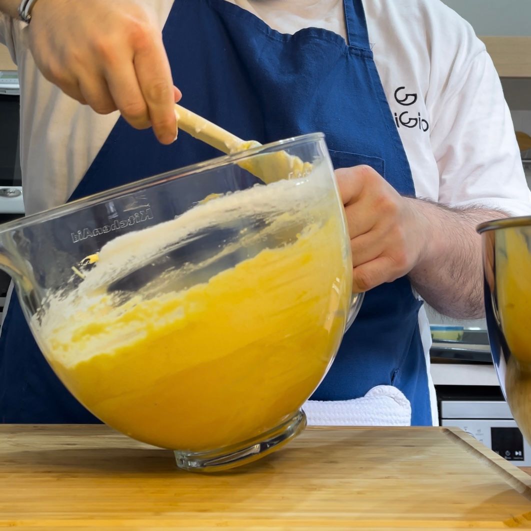 Un uomo con un grembiule sta mescolando qualcosa in una ciotola di vetro