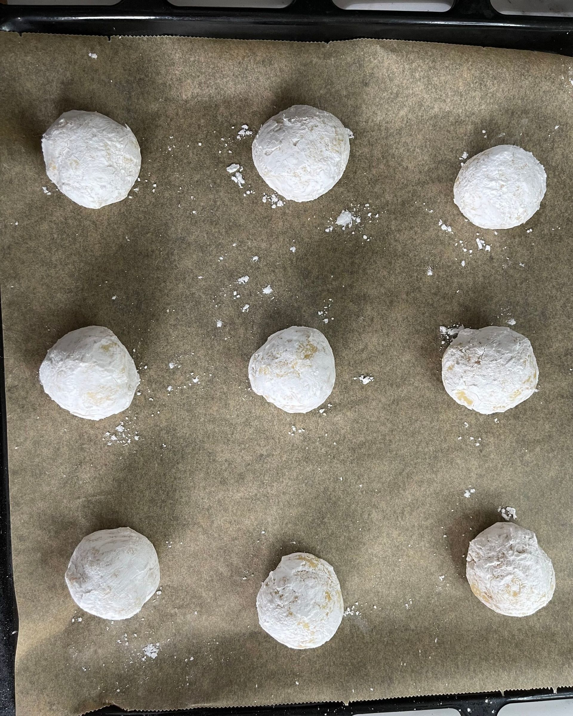 Una teglia piena di biscotti ricoperti di zucchero a velo su una teglia da forno.