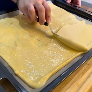 Una persona sta usando una spatola per stendere una sostanza gialla su un vassoio