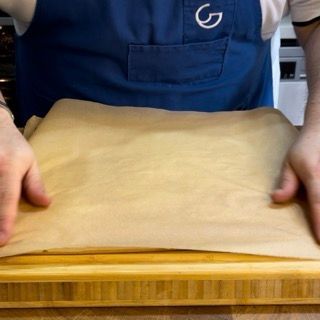 Una persona con un grembiule blu tiene in mano un pezzo di carta marrone