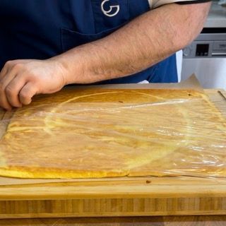 Un uomo con un grembiule blu sta tagliando un pezzo di cibo su un tagliere di legno