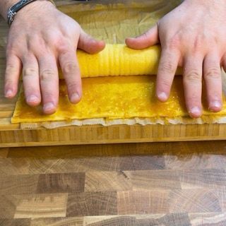 Una persona sta facendo rotolare un pezzo di cibo su un tagliere di legno