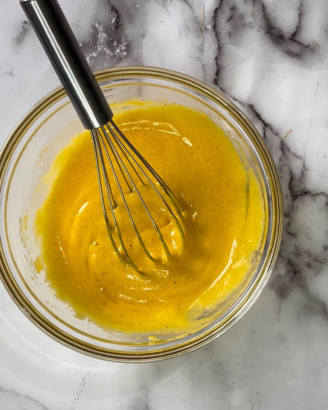 Una ciotola di liquido giallo con una frusta dentro