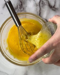 Una persona tiene in mano una frusta in una ciotola piena di liquido giallo.