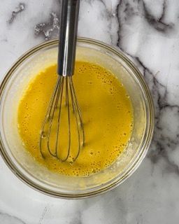 Una ciotola di liquido giallo con una frusta dentro.