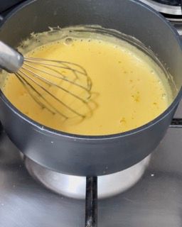 Una pentola con del liquido giallo e una frusta dentro.