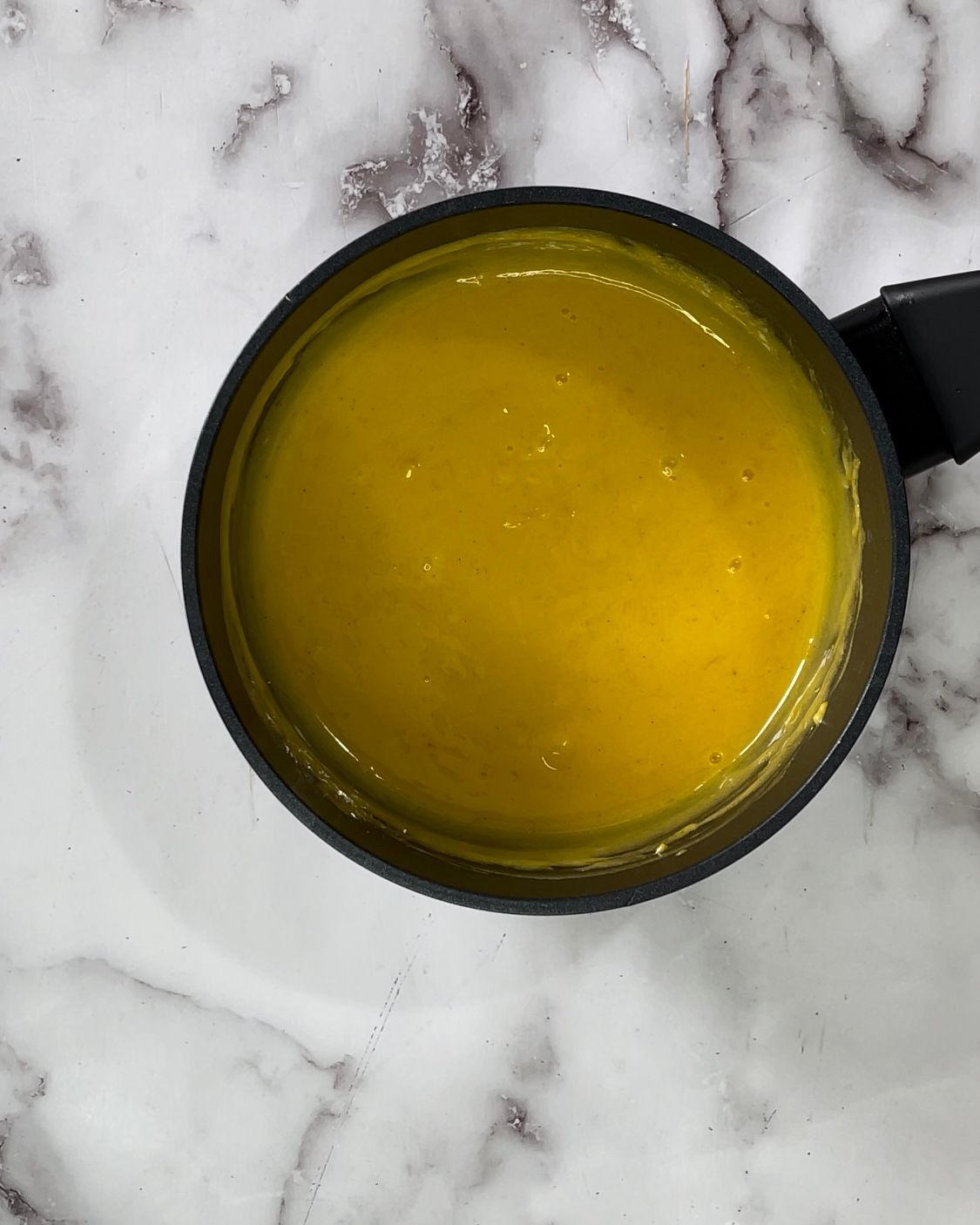 Una tazza di liquido giallo è appoggiata su una superficie di marmo.