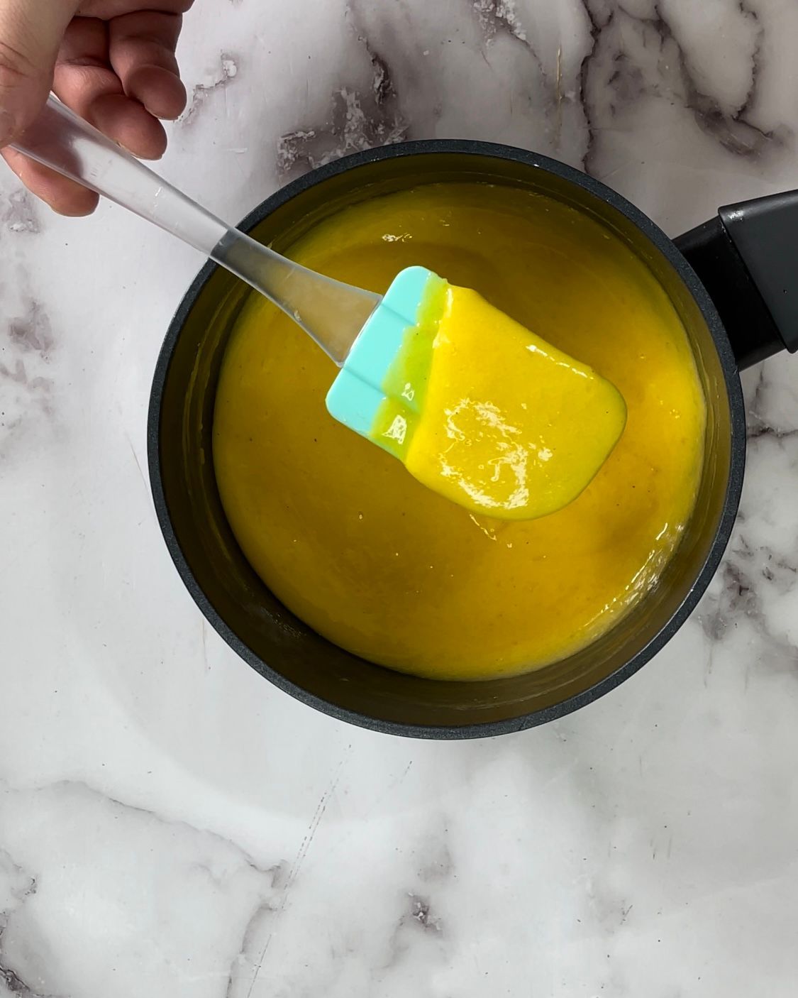 Una persona tiene una spatola sopra una pentola piena di liquido giallo.