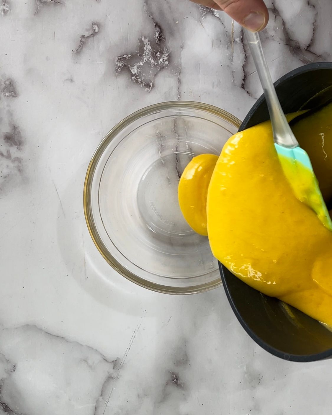 Una persona versa del liquido giallo in una ciotola con una spatola.