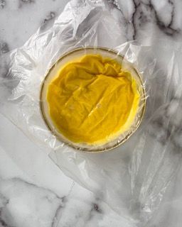 Una ciotola di salsa gialla è avvolta nella pellicola trasparente su una superficie di marmo.