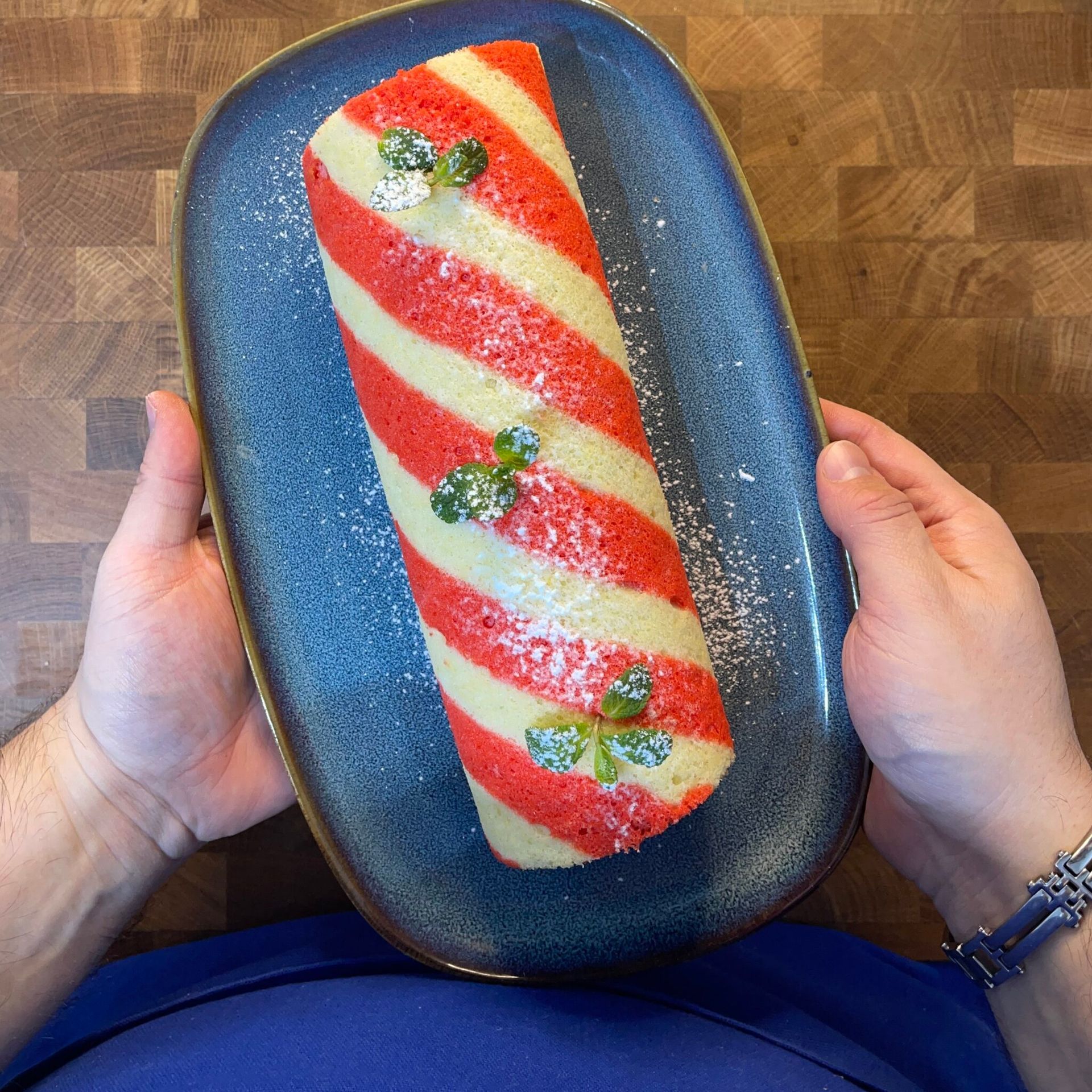 Una persona tiene in mano un piatto blu con sopra una torta a strisce rosse e bianche.