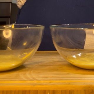 Due ciotole di liquido sono appoggiate su un tavolo di legno.